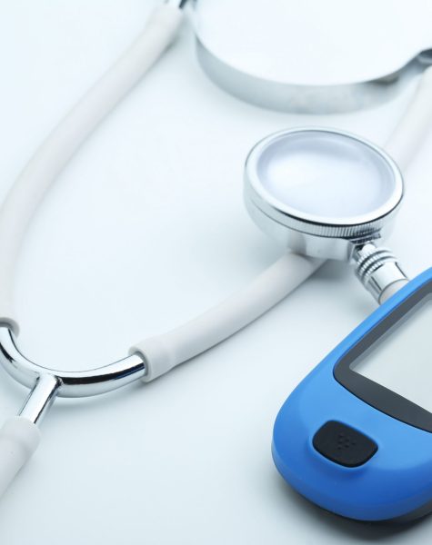 Blood glucose meter and stethoscope on white background